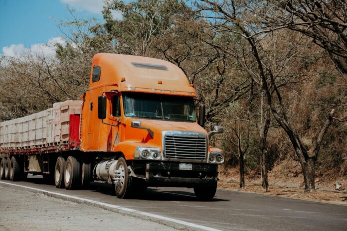 Paro de Los Pachenca: hasta 3.000 camiones quietos en la Troncal del Caribe y una factura de $81.000 millones, según Fedetranscarga Tractocamión naranja con carga en una carretera bordeada de árboles secos