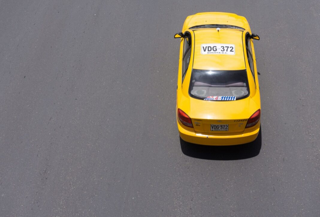 Taxi amarillo con placas de Bogotá visto desde arriba sobre una vía vacía