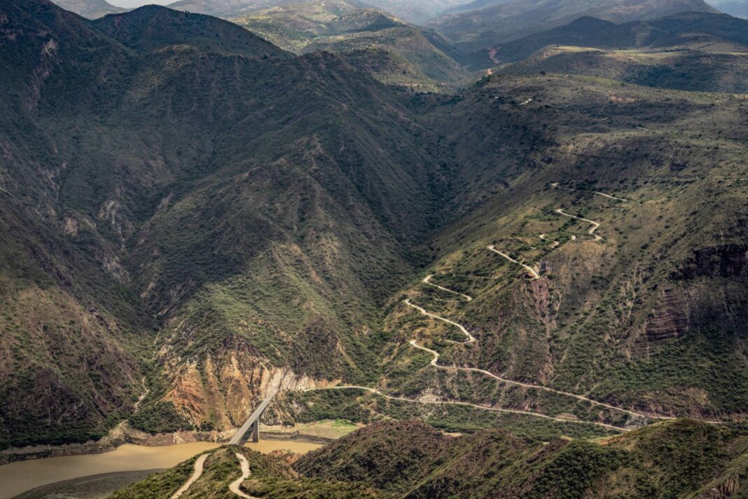 Carretera en zigzag que baja a un puente sobre un río en un valle andino
