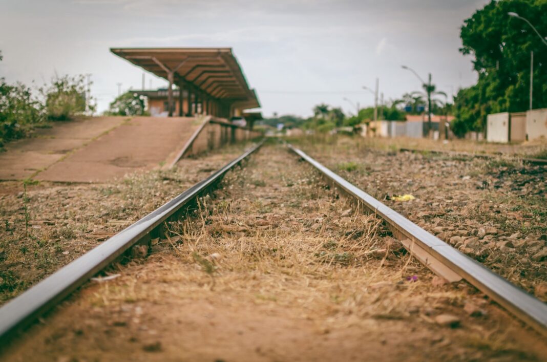 Vía férrea con pasto seco junto a un andén techado de una estación sin movimiento en Brasil