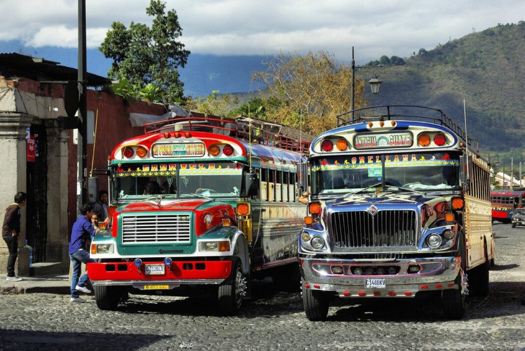 Dos autobuses extraurbanos decorados estacionados en una calle empedrada de Antigua Guatemala