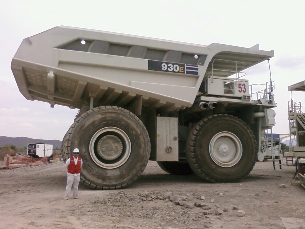 Camión minero Komatsu 930E de tracción eléctrica junto a un trabajador con casco