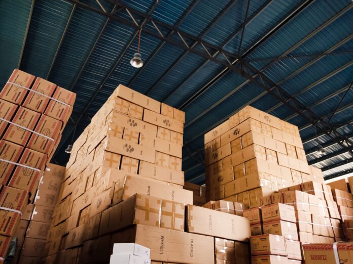 La Aduana argentina devuelve el courier a Ezeiza: los depósitos fiscales privados tienen 30 días para dejar de operar envíos Pilas de cajas de cartón en un depósito con techo de chapa azul