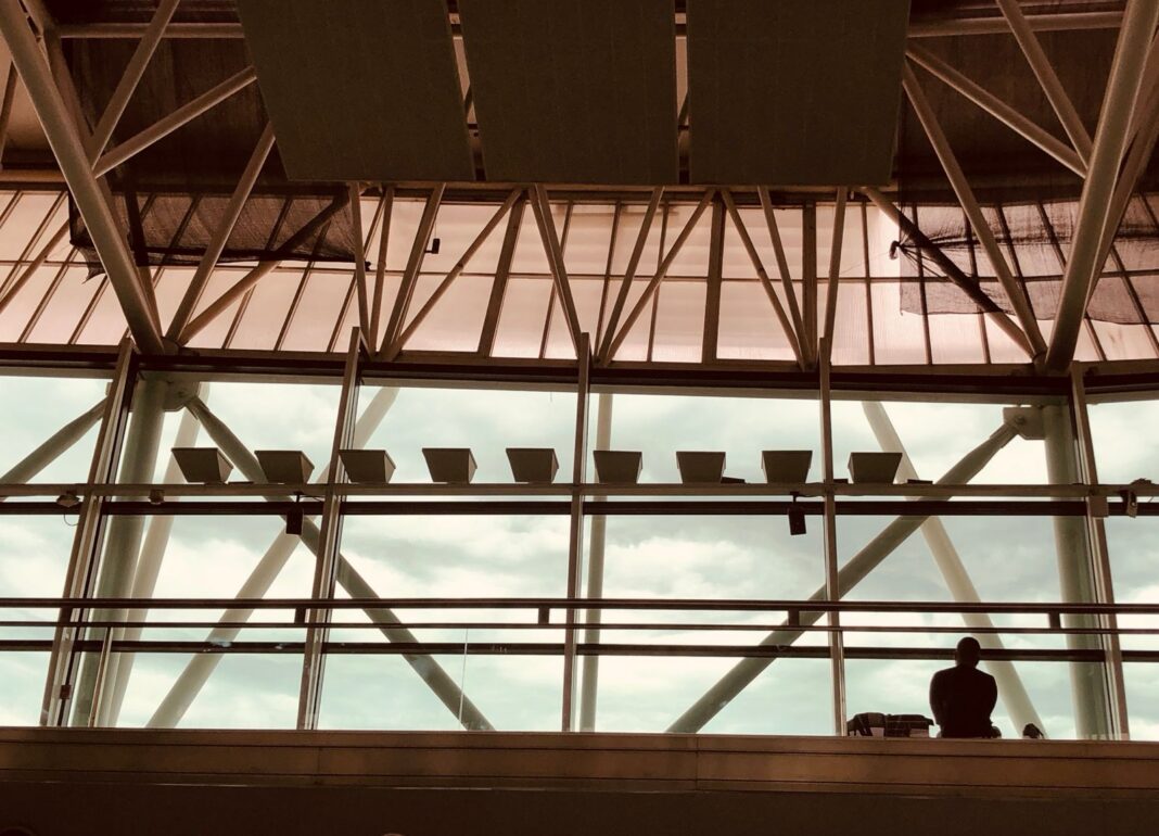 Interior de la terminal del aeropuerto de Ezeiza con su estructura metálica y un pasajero junto al ventanal