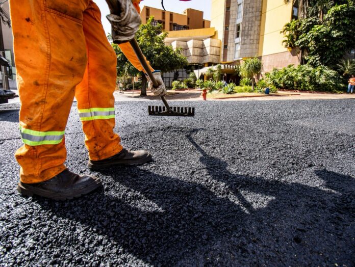 Alliana reasigna G. 134.816 millones a rutas, dragado y un hospital, y un diario eleva la cuenta a G. 180.000 millones Trabajador con uniforme naranja extendiendo asfalto nuevo con un rastrillo
