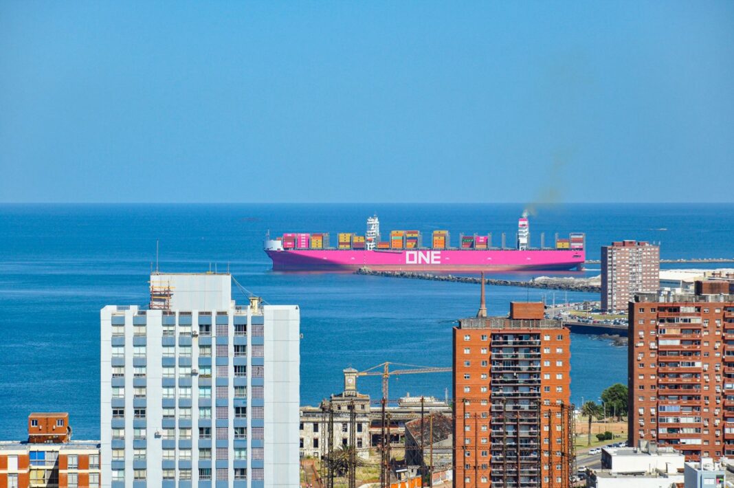 Buque portacontenedores entrando al puerto de Montevideo, visto entre edificios de la ciudad