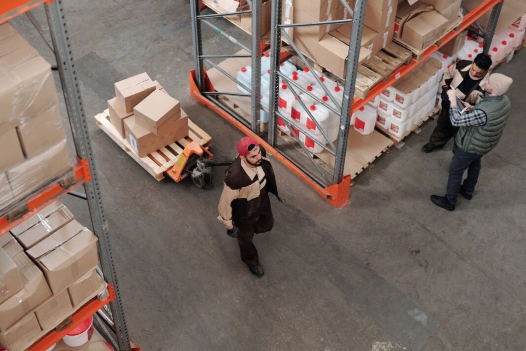 Trabajador de un almacén logístico arrastra un palé con una transpaleta entre estanterías