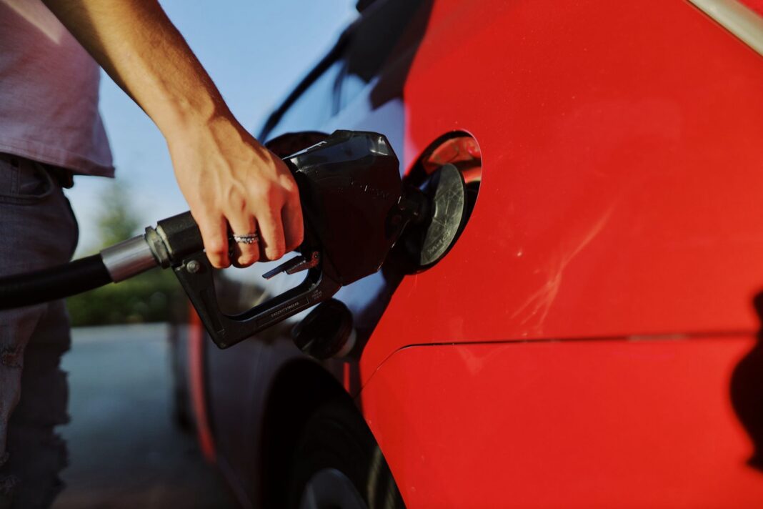 Mano sosteniendo una pistola de combustible al cargar un auto rojo