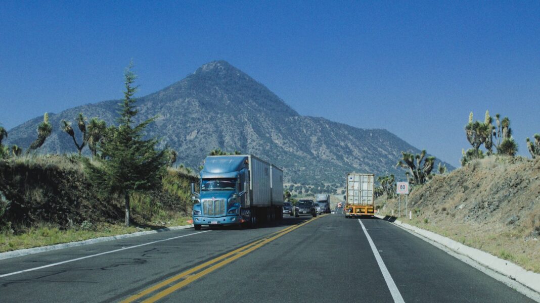 Tractocamiones circulan por una carretera de dos carriles entre palmas yuca y un cerro en el centro de México