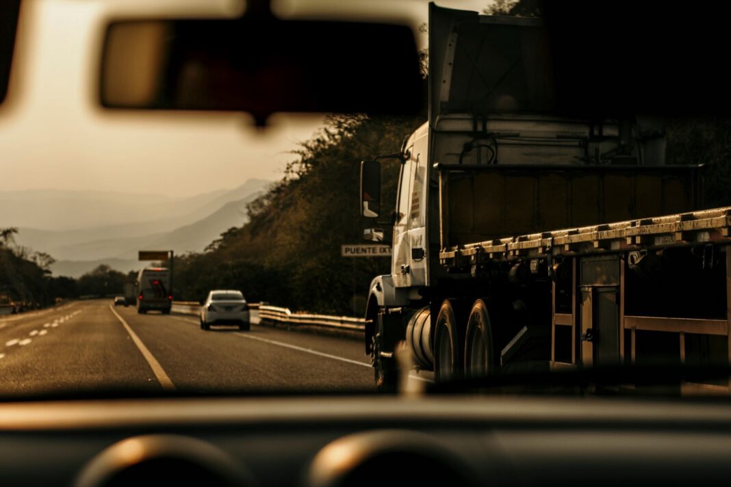 Tractocamión con plataforma en una carretera de montaña en México, visto desde el interior de un auto al atardecer