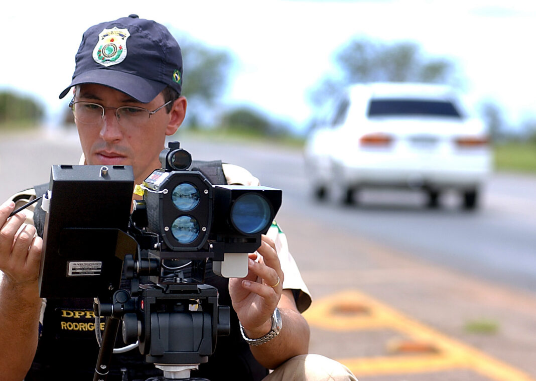 Agente de la policía de carreteras de Brasil operando un radar de velocidad sobre un trípode junto a una carretera