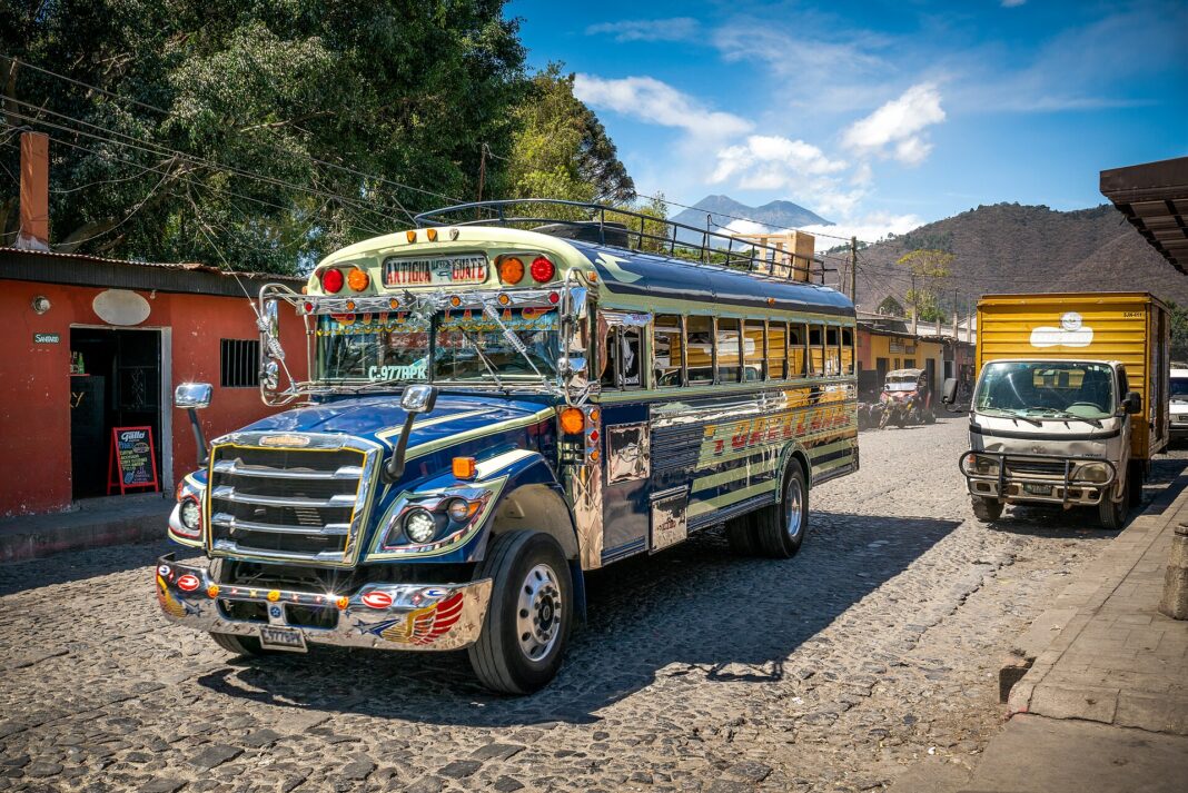 Camioneta extraurbana decorada y un camión de carga en una calle empedrada de Antigua Guatemala