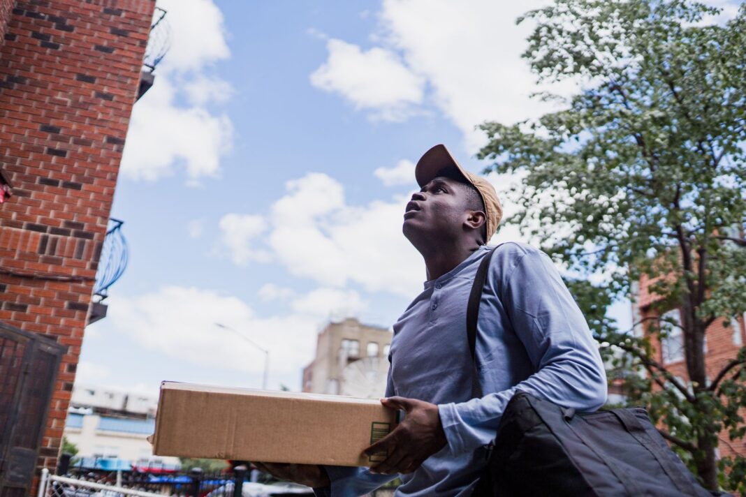 Repartidor con una caja busca la dirección frente a un edificio de departamentos