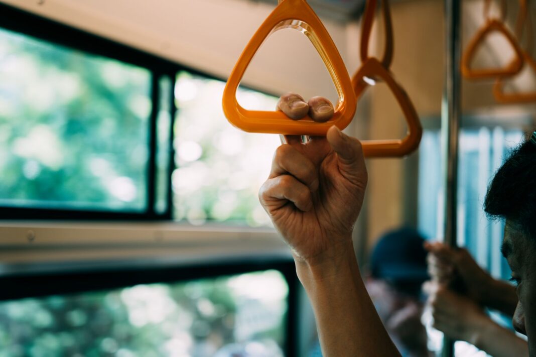 Pasajero de pie sujeta la agarradera dentro de un autobús urbano