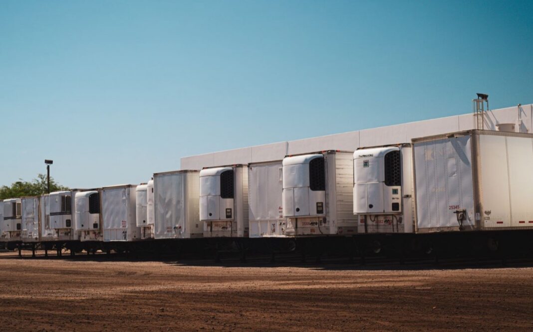 Fila de remolques refrigerados estacionados en un patio de tierra junto a una nave industrial