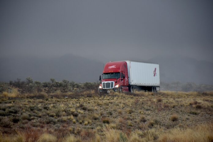 EE. UU. exime 5 años a camiones autónomos de usar triángulos Tractocamión rojo con remolque blanco en una carretera del desierto bajo un cielo de tormenta