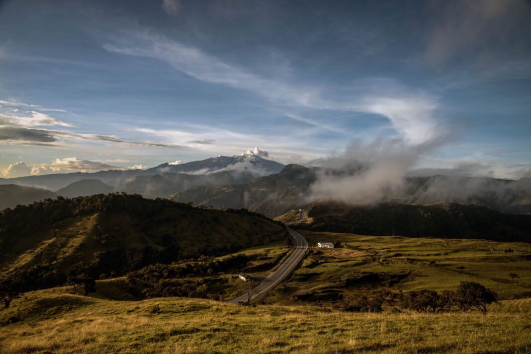 Carretera de dos carriles que serpentea entre colinas verdes de los Andes colombianos, con un nevado al fondo