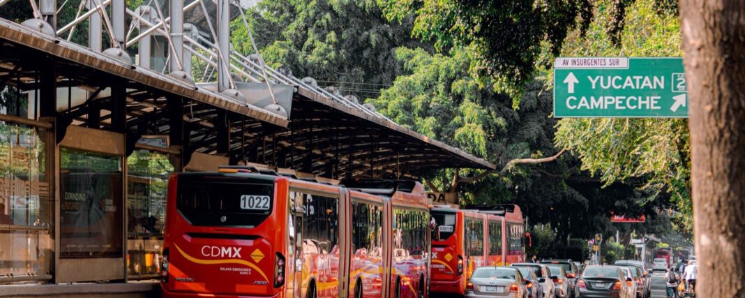 Dos autobuses articulados rojos del Metrobús detenidos en una estación techada de avenida Insurgentes, entre árboles