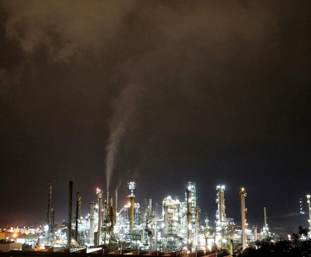 Refinería de Enap en Concón iluminada de noche, con sus torres y chimeneas bajo un cielo nublado