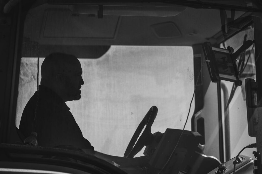 Silueta de un operador al volante dentro de la cabina de un camión, en blanco y negro
