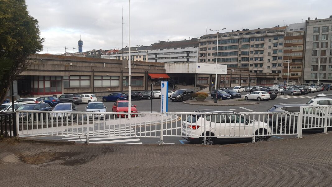 Fachada de la actual estación de autobuses de A Coruña, en Cuatro Caminos, con coches aparcados delante y edificios de viviendas al fondo