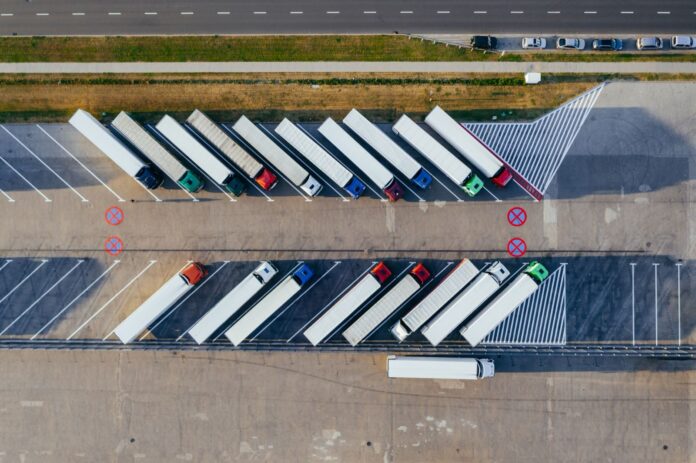 España: el diésel baja a 1,889 € y la rebaja de 20 céntimos sigue Tractocamiones con semirremolque estacionados en diagonal en un aparcamiento, vistos desde arriba