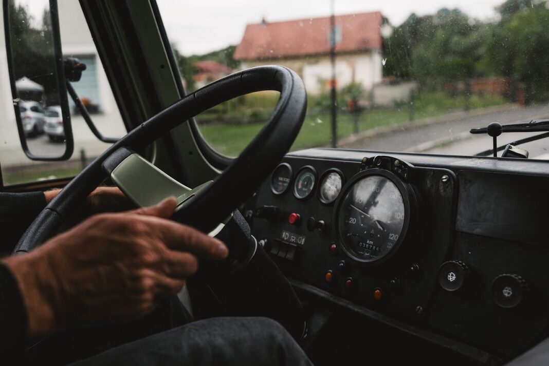 Manos de un conductor veterano en el volante de un camión, con el tacómetro en kilómetros