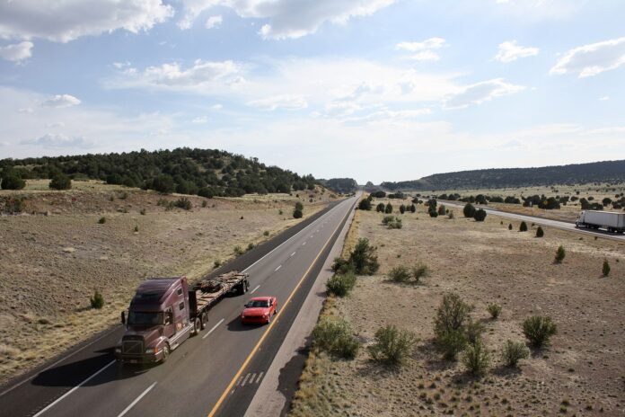 Fletes en EE. UU.: embarcadores pagan 32,1% más por igual carga Tractocamión con plataforma y un auto circulan por la Interestatal 40 en una llanura semidesértica de Arizona