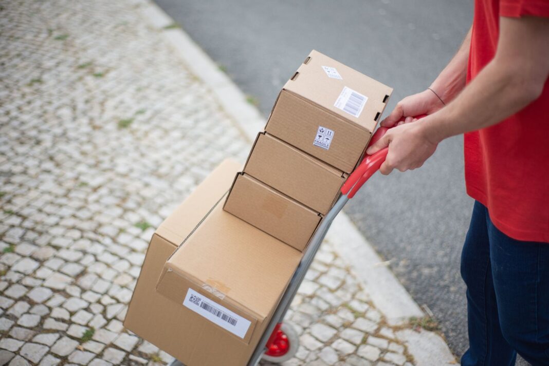 Repartidor empuja por la acera una carretilla cargada con cajas de paquetería