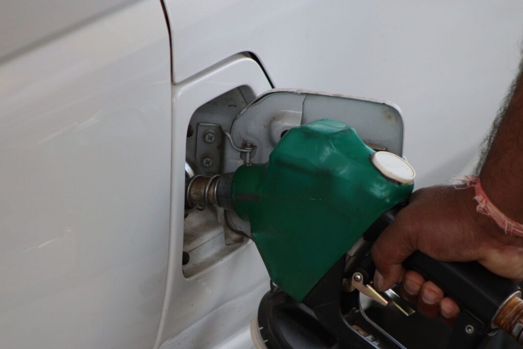 Mano sostiene una pistola de combustible verde mientras carga el tanque de un vehículo blanco
