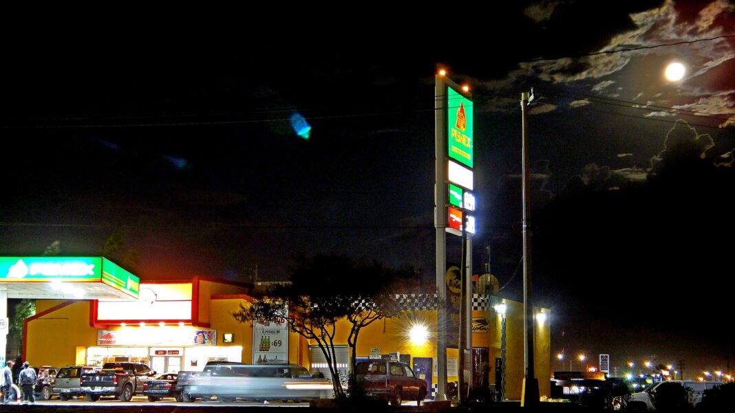 Gasolinera Pemex de noche con su anuncio de precios iluminado y camionetas estacionadas