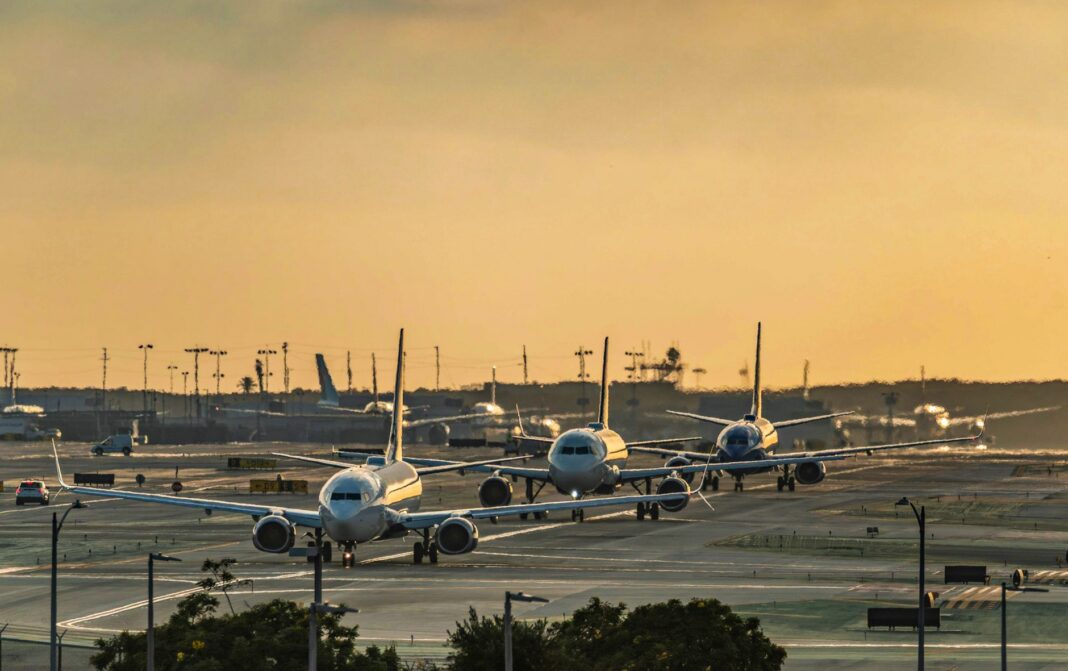 Varios aviones comerciales en fila sobre la pista de rodaje de un aeropuerto al atardecer