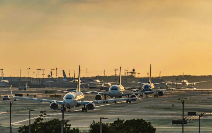 Nueva York: la FAA da a JetBlue 22 slots de Spirit en LaGuardia Varios aviones comerciales en fila sobre la pista de rodaje de un aeropuerto al atardecer