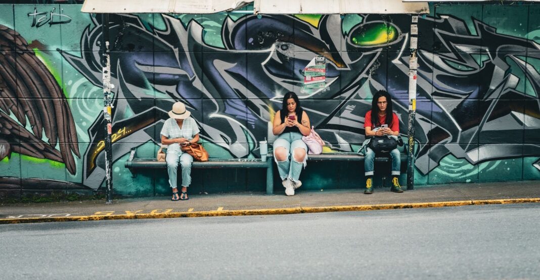 Tres personas esperan el bus en una parada con grafitis en San José, Costa Rica
