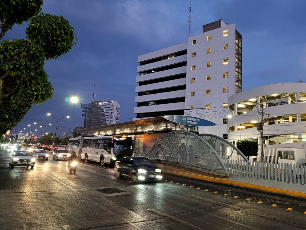 Autobús articulado del SIT de León sale de la estación Central Camionera al anochecer, entre autos y motos