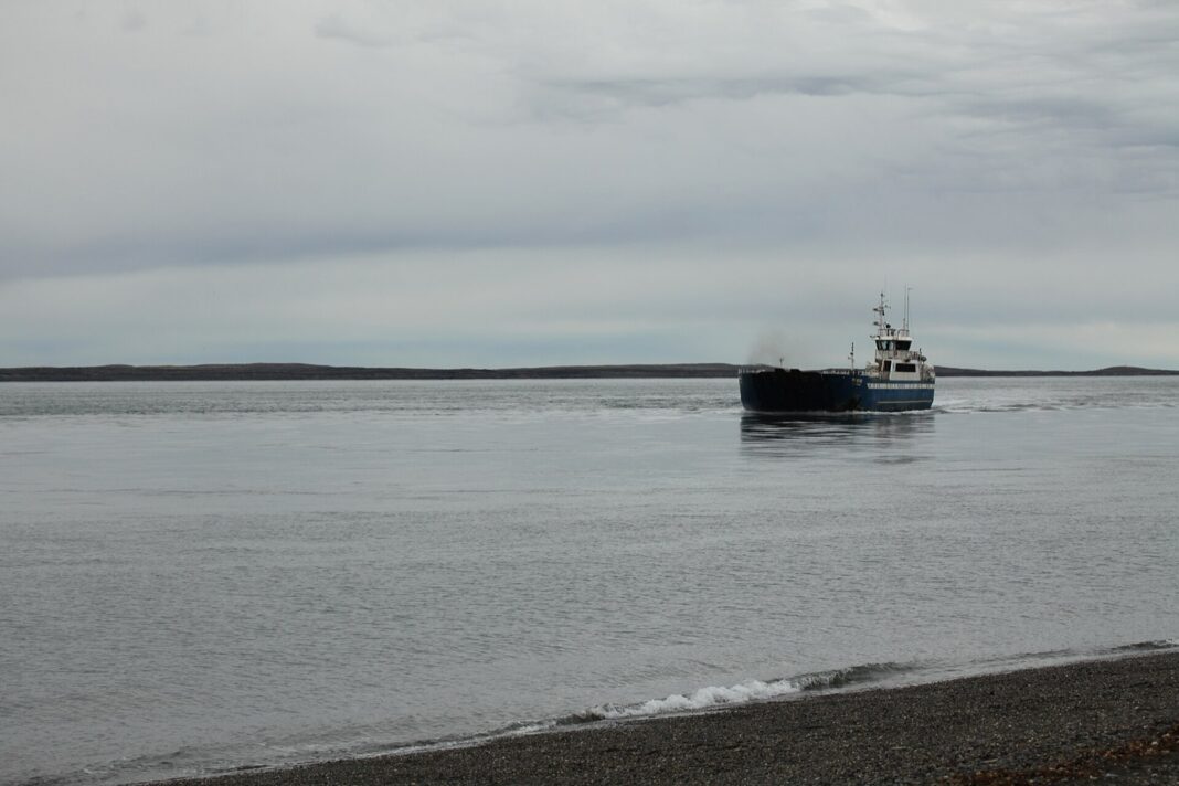 Transbordador de carga navega por el estrecho de Magallanes bajo un cielo gris, cerca de la costa