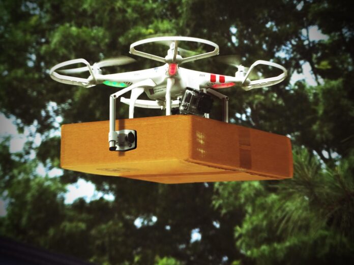 Medellín: primer vuelo de carga con dron cubre 5,5 km en 5 min Dron cuadricóptero blanco en vuelo con una caja de cartón sujeta debajo
