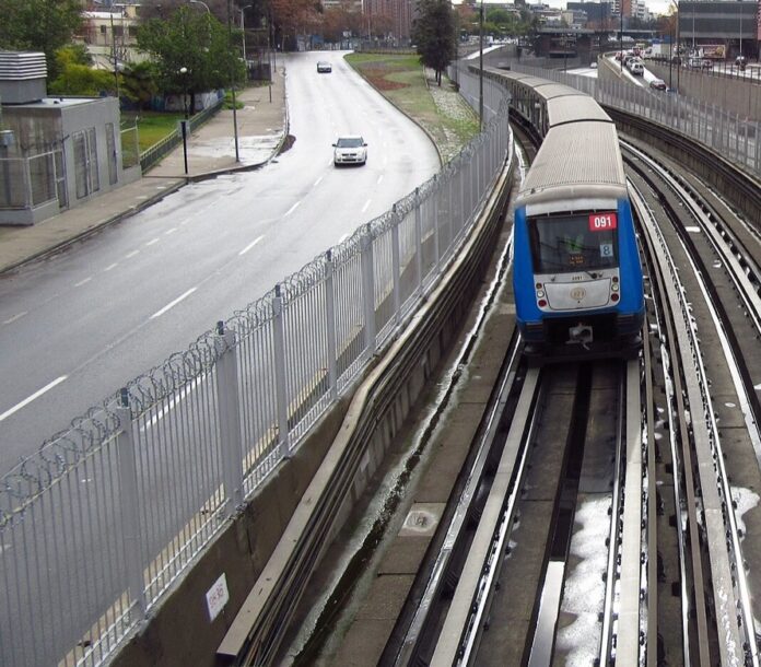 Metro de Santiago: la tormenta parte la L2 en dos por horas Tren de la Línea 2 del Metro de Santiago en superficie sobre vías mojadas, junto a una avenida con pavimento húmedo