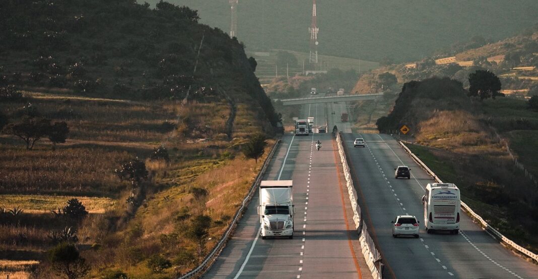 Tractocamión y autobús circulan por una autopista de cuatro carriles entre cerros en México