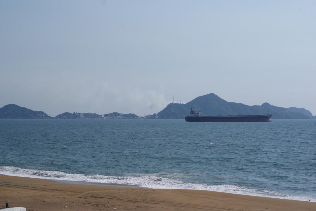 Buque granelero fondeado frente a la playa de Manzanillo, con los cerros y la ciudad al fondo