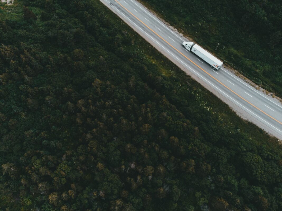 Tractocamión circula por una carretera rodeada de selva vista desde un dron