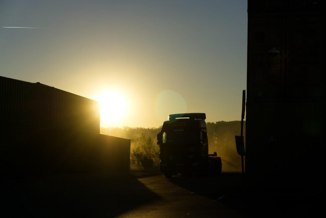 Tractocamión a contraluz entre contenedores apilados en un patio de carga al amanecer