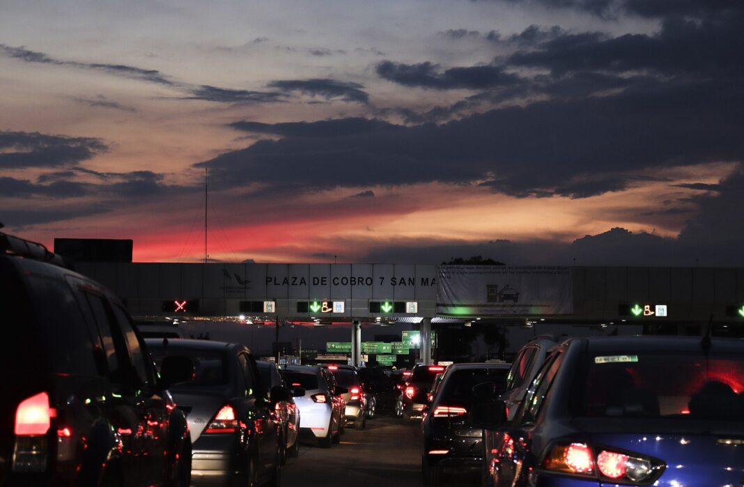 Fila de autos al atardecer frente a la plaza de cobro San Marcos de la autopista México-Puebla, con carriles de telepeaje IAVE