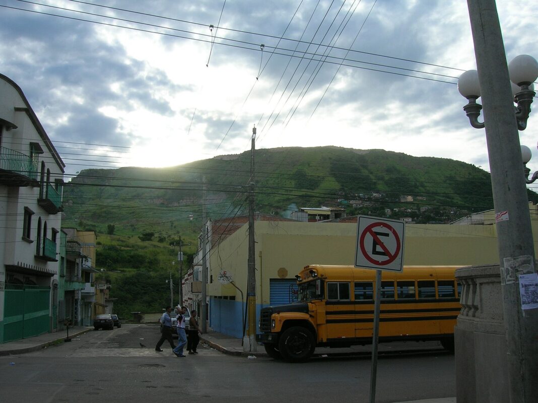 Bus amarillo de transporte colectivo en una calle de Tegucigalpa con un cerro al fondo